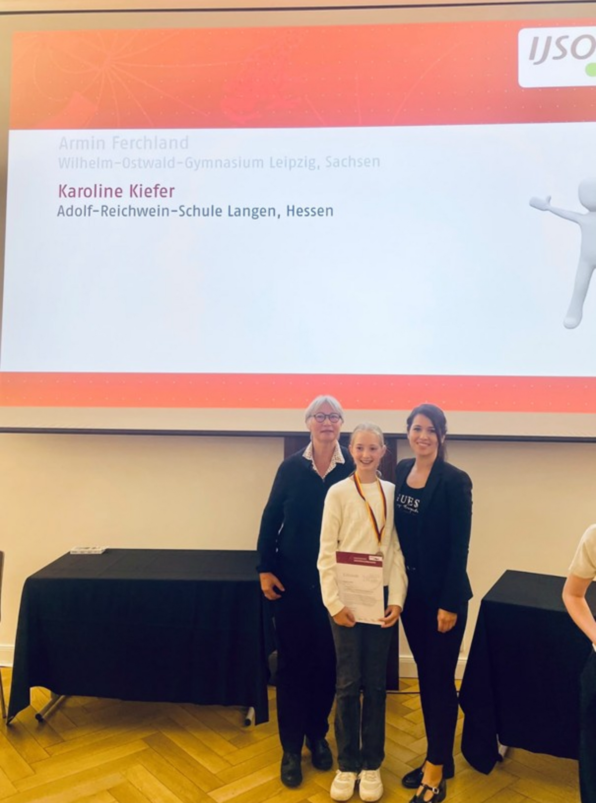 Die elfjährige Karoline Kiefer präsentiert ihre Urkunde, die sie beim Bundesfinale der Internationalen JuniorScience Olympiade (IJSO) in Oldenburg für ihre erfolgreiche Teilnahme erhielt. Neben ihr stehen Dr. Esther von Estorff (links) und Sinem Mutaf (rechts)