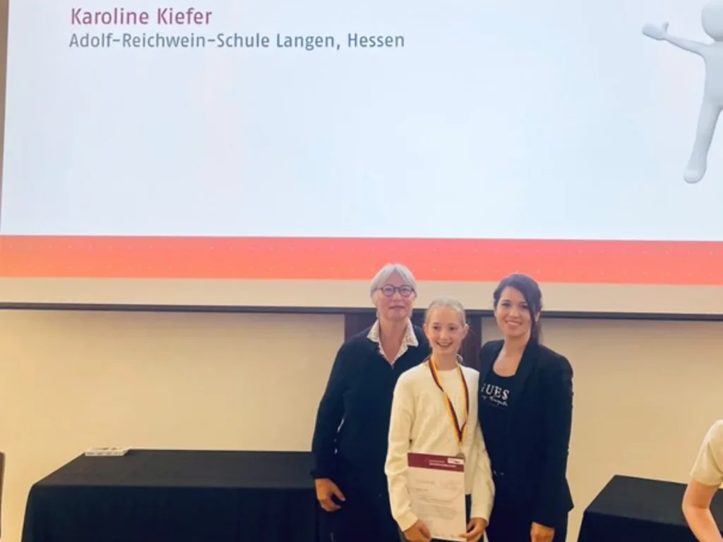 Die elfjährige Karoline Kiefer präsentiert ihre Urkunde, die sie beim Bundesfinale der Internationalen JuniorScience Olympiade (IJSO) in Oldenburg für ihre erfolgreiche Teilnahme erhielt. Neben ihr stehen Dr. Esther von Estorff (links) und Sinem Mutaf (rechts)