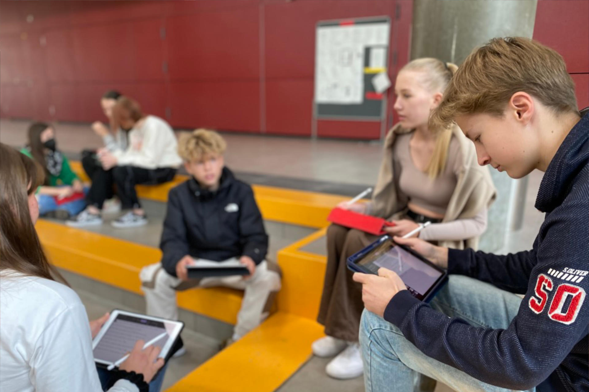 Schülergruppe sitzt mit iPads in der Aula und lernt. FOTO: Andreas Wolf