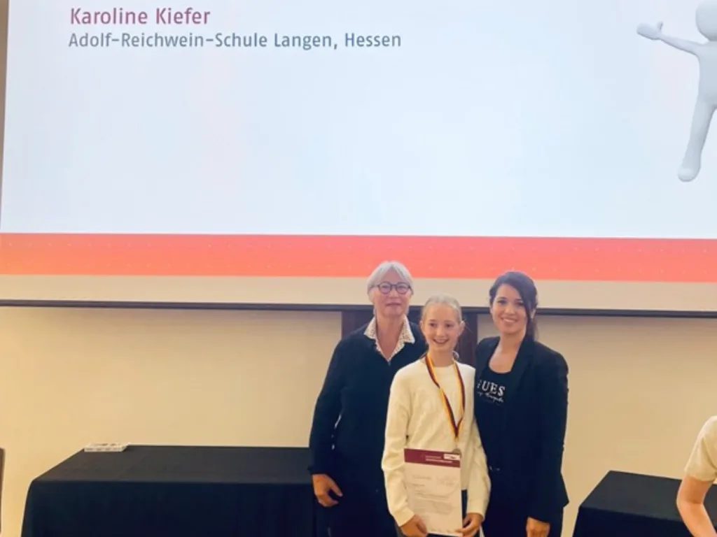 Die elfjährige Karoline Kiefer präsentiert ihre Urkunde, die sie beim Bundesfinale der Internationalen JuniorScience Olympiade (IJSO) in Oldenburg für ihre erfolgreiche Teilnahme erhielt. Neben ihr stehen Dr. Esther von Estorff (links) und Sinem Mutaf (rechts)