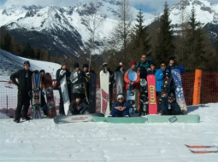 Eine Gruppe Jugendlicher steht mit Skiern und Snowboards am Rand einer Piste im Ahrntal, dahinter verschneite Berge und Nadelwald.