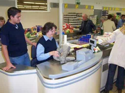 Ein Praktikant steht an der Kasse eines Supermarkts neben einer Mitarbeiterin.