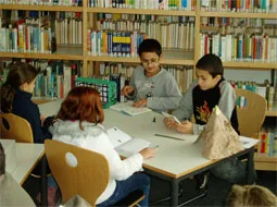 Ältere und jüngere Kinder sitzen gemeinsam an einem Tisch in der Bücherei.