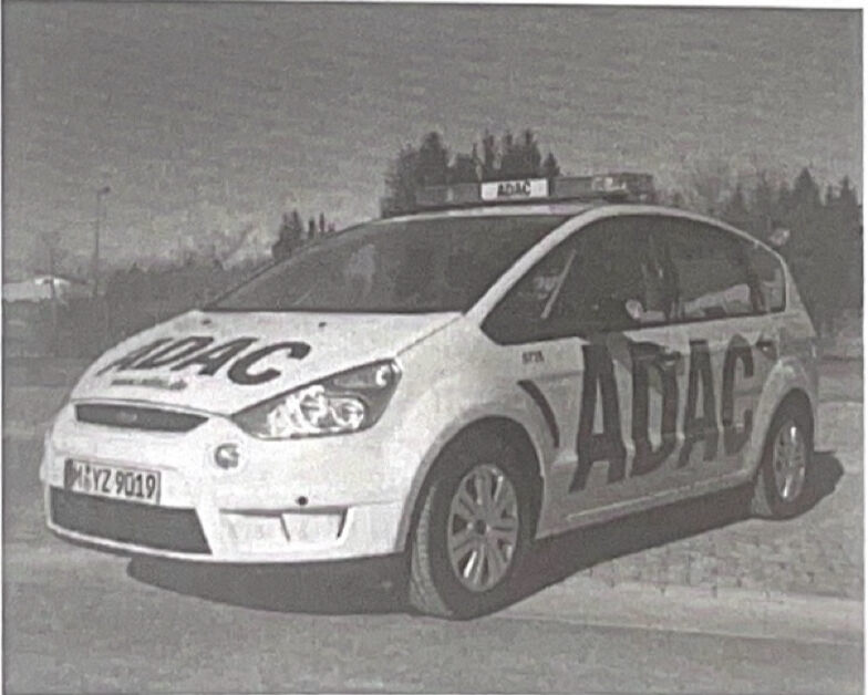 Ein weißes Fahrzeug mit großer „ADAC“-Beschriftung und Dachschild steht auf einem Platz (Schwarz-Weiß-Aufnahme).