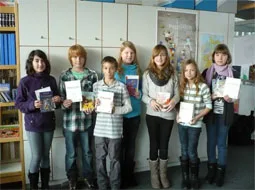 Kinder halten im Klassenraum ihre Urkunden und Buchpreise in die Kamera.