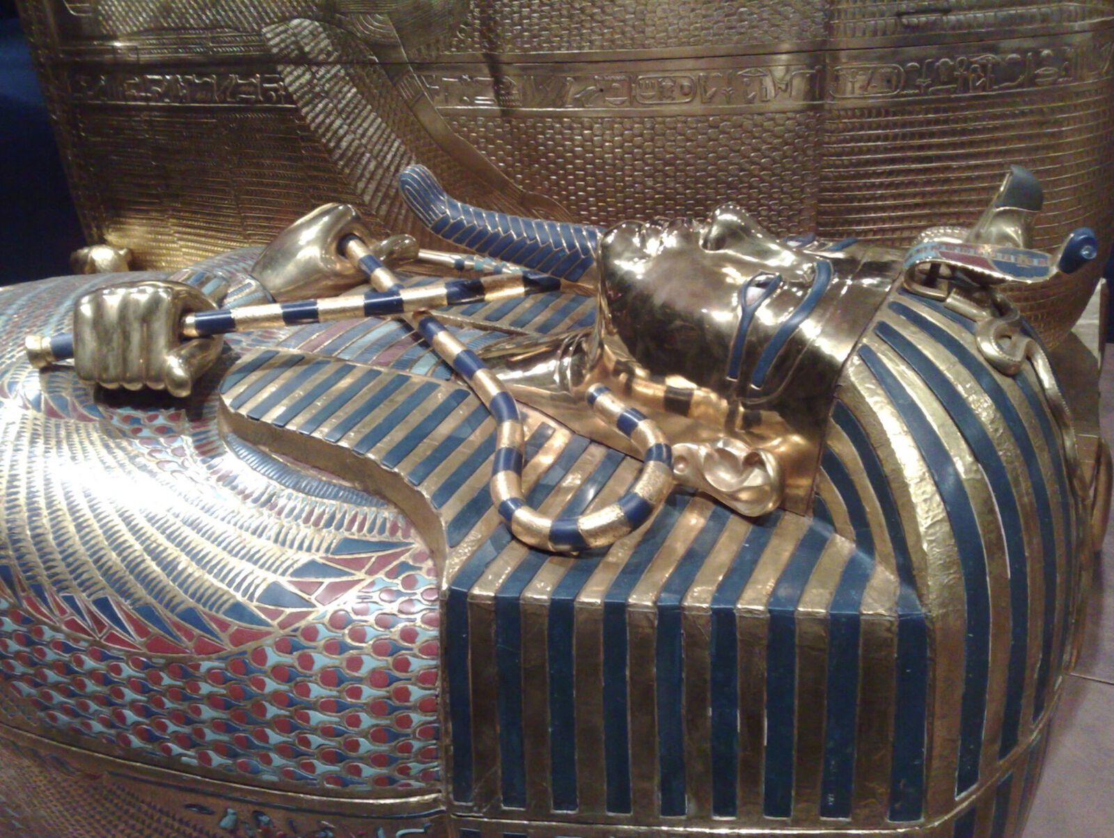 Ein goldener ägyptischer Sarkophag im Stil des Tutanchamun mit überkreuzten Armen, die Krummstab und Wedel halten, sowie blau-goldenem Kopftuch.