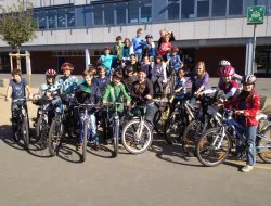 Die Radgruppe steht mit Fahrrädern und Helmen vor dem Schulgebäude.