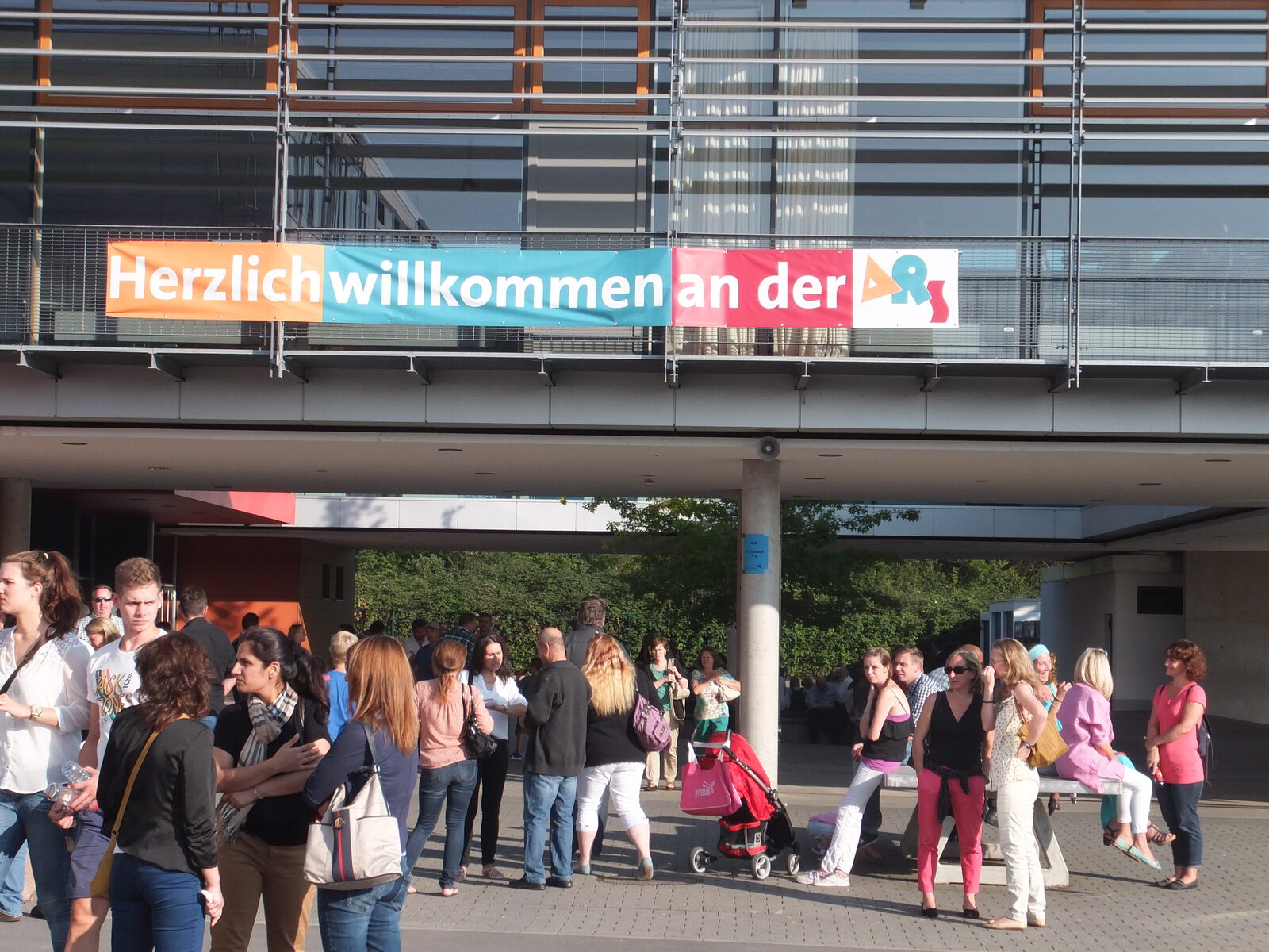 Eltern und Familien versammeln sich im Schulhof unter dem Banner „Herzlich willkommen an der ARS“ zur Einschulungsfeier.