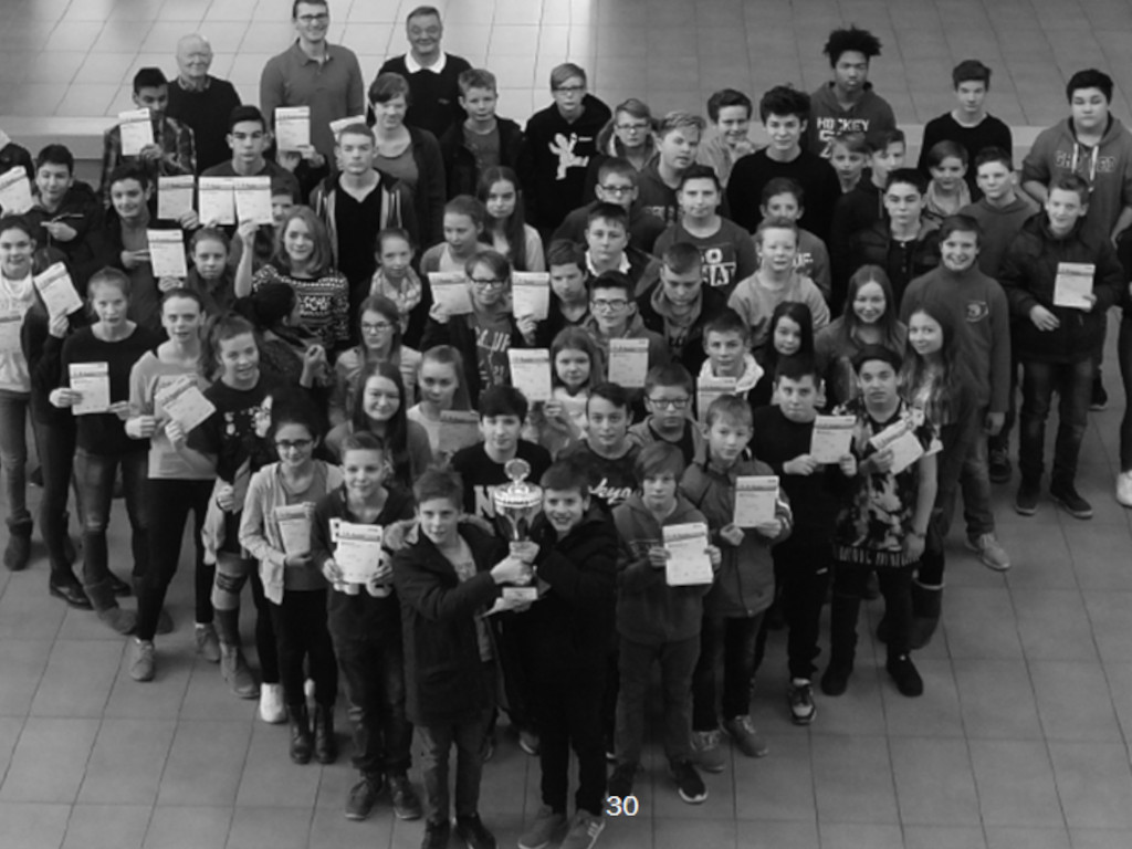 Eine große Schülergruppe hält Sportabzeichen-Urkunden hoch; in der Mitte wird ein Pokal in die Höhe gehalten, daneben Lehrkräfte (Schwarz-Weiß-Aufnahme).