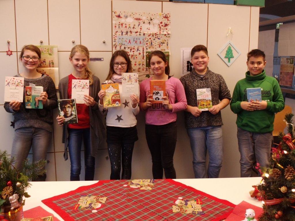 Sechs Kinder halten Urkunden und Bücher in die Kamera; davor ein weihnachtlich geschmückter Tisch mit Tannenzweigen.
