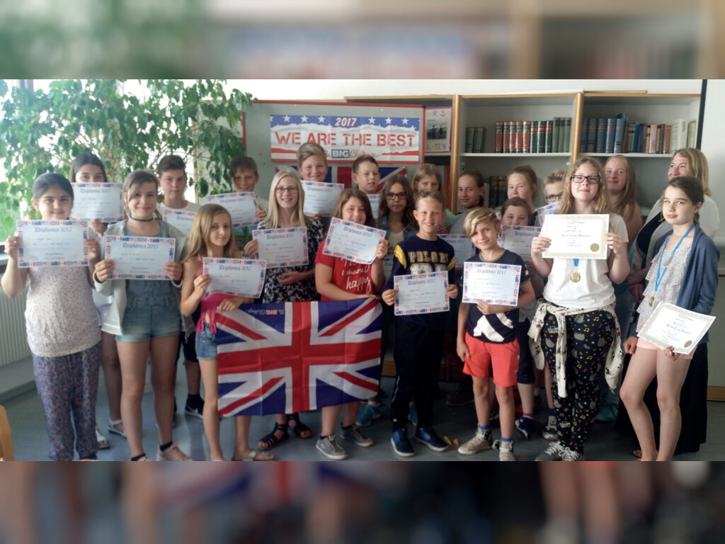 Eine große Gruppe Kinder hält „Diploma 2017“-Urkunden und eine britische Flagge in die Kamera; im Hintergrund ein Banner mit der Aufschrift „We are the best 2017“.