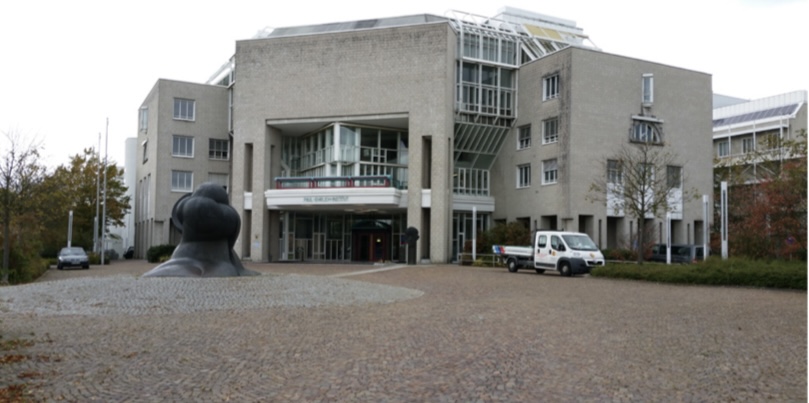 Das Gebäude des Paul-Ehrlich-Instituts von außen: ein großer heller Klinkerbau mit gepflastertem Vorplatz und einer abstrakten Bronzeskulptur.