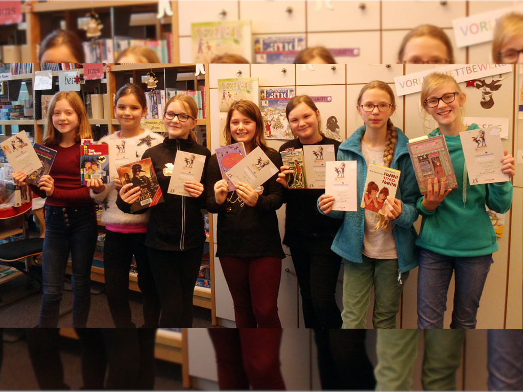 Sieben Kinder halten Bücher und Urkunden in die Kamera; im Hintergrund Bücherregale und ein „Vorlesewettbewerb“-Plakat in der Schulbücherei.
