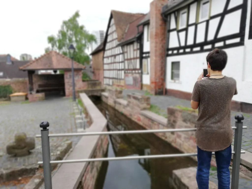 Jugendlicher fotografiert am Bachlauf vor Fachwerkhäusern.