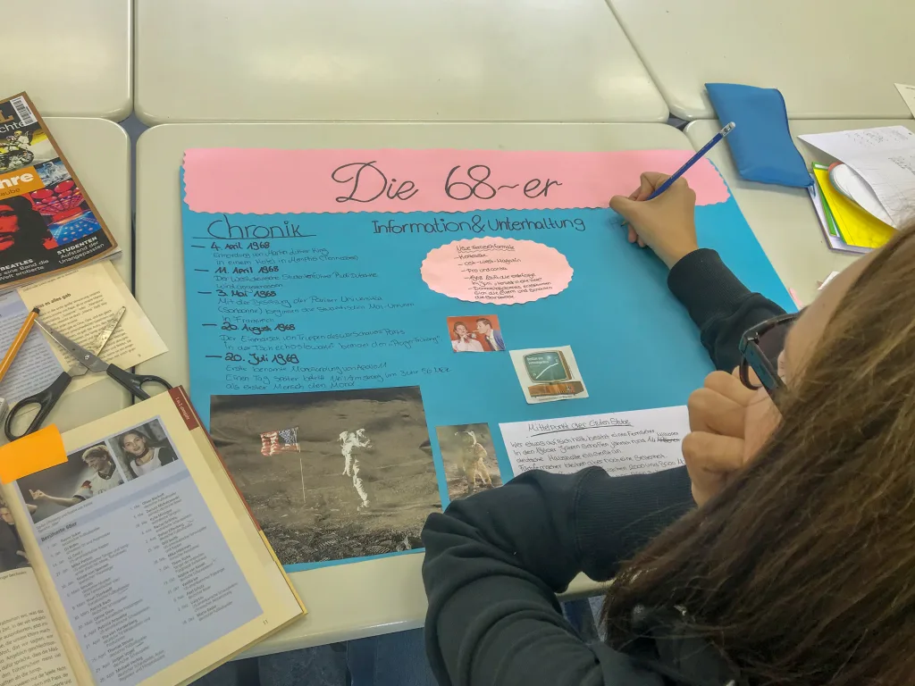 Person beschriftet ein Plakat mit der Überschrift „Die 68er“.