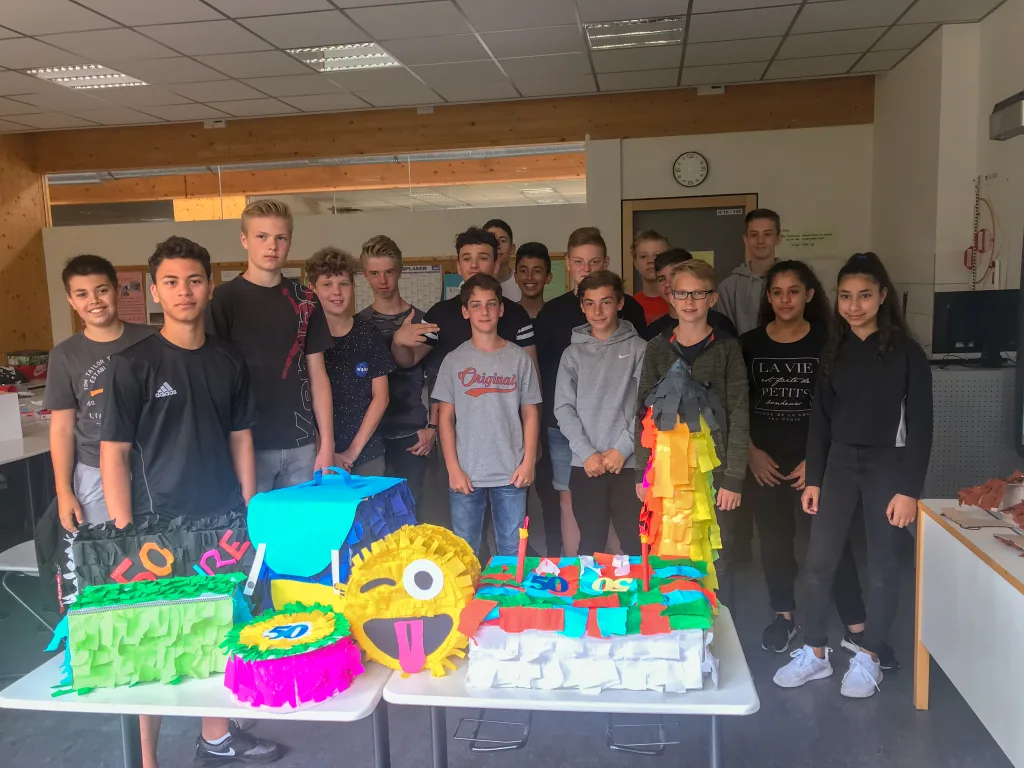 Klassengruppe steht hinter einem Tisch mit selbst gebauten Piñatas.