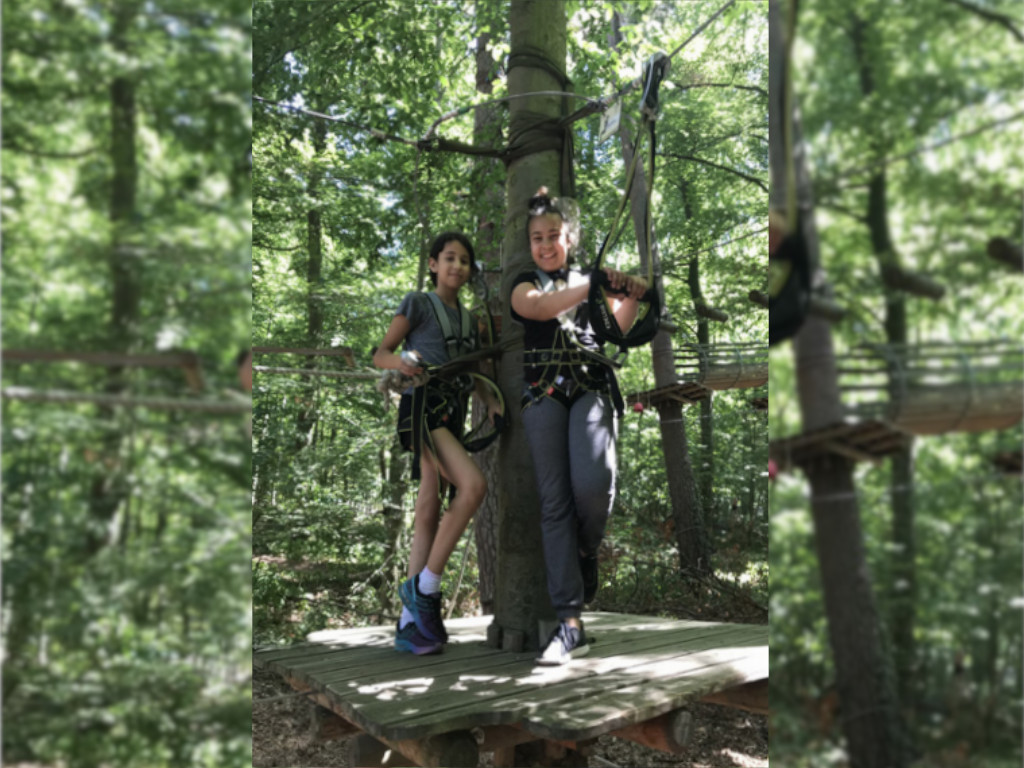Jugendliche stehen auf einer Holzplattform im Kletterwald und blicken mit ihrer Kletterausrüstung in die Kamera.
