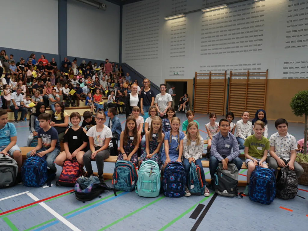 Neue fünfte Klasse sitzt mit Schulranzen auf dem Hallenboden.