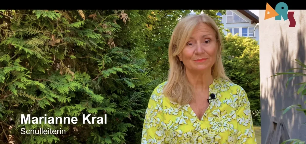 Standbild aus dem Abschiedsvideo: die Schulleiterin steht vor Bäumen und spricht in die Kamera.