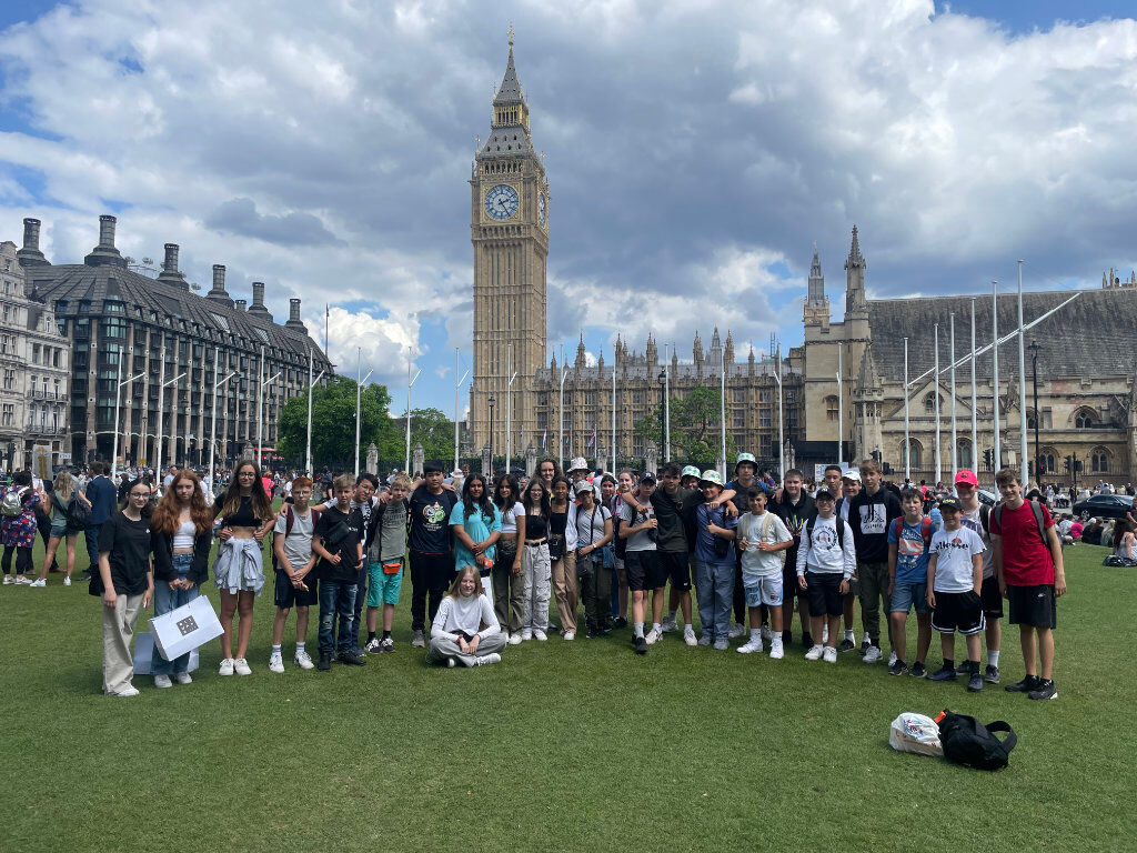 Eine große Schülergruppe posiert auf einer Rasenfläche vor dem Big Ben und den Houses of Parliament in London.