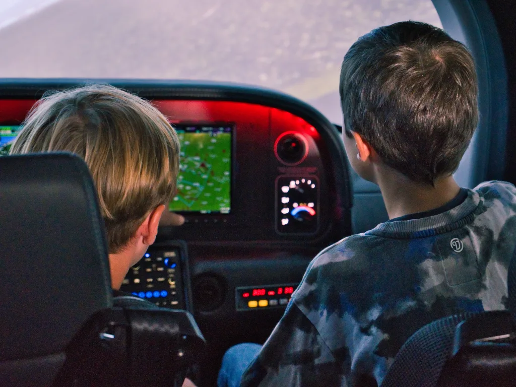 Zwei Jugendliche sitzen im Cockpit eines Kleinflugzeugs vor den Bildschirmen.