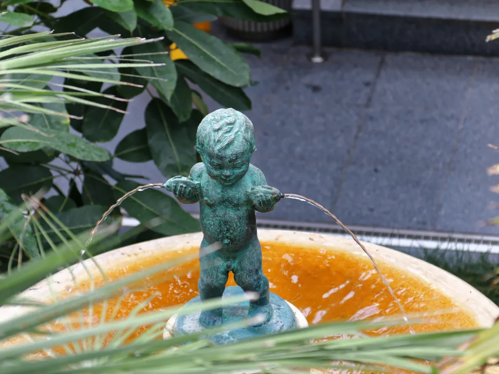Bronzefigur eines Kindes als Wasserspeier über einer Brunnenschale.
