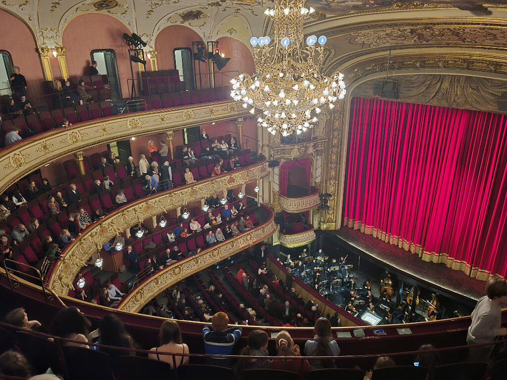 Der prunkvolle Zuschauerraum der Staatsoper Wiesbaden mit rotem Bühnenvorhang, goldverzierten Rängen, großem Kronleuchter und dem Orchestergraben.