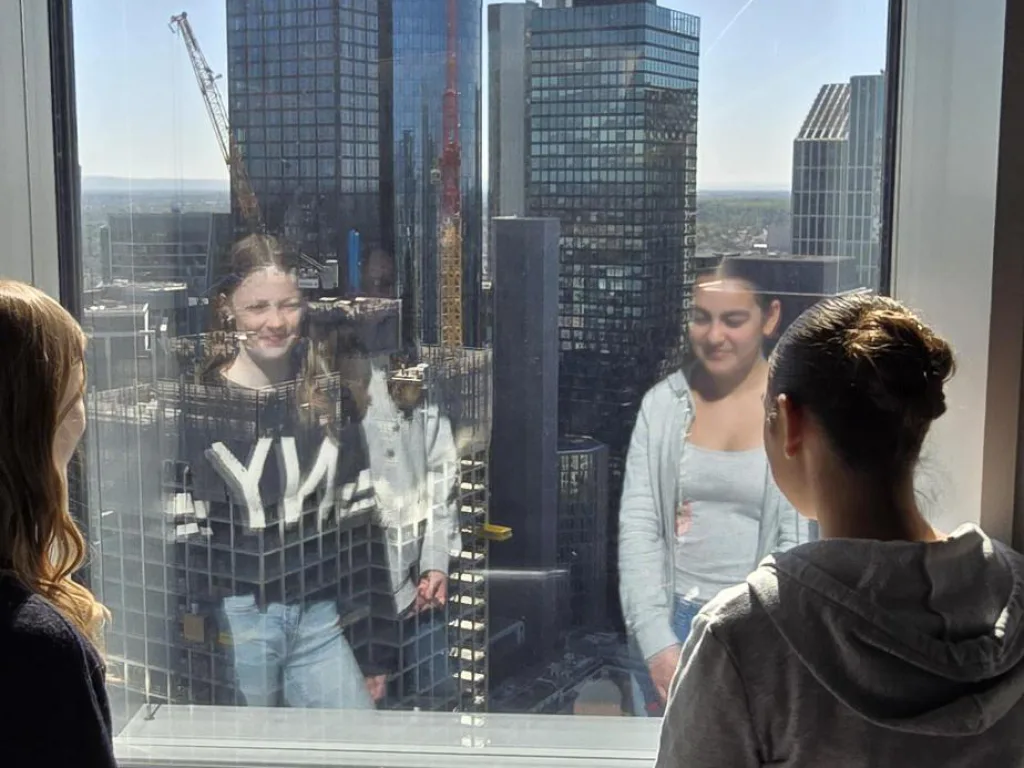 Jugendliche stehen an einer Fensterfront, dahinter die Frankfurter Hochhäuser.