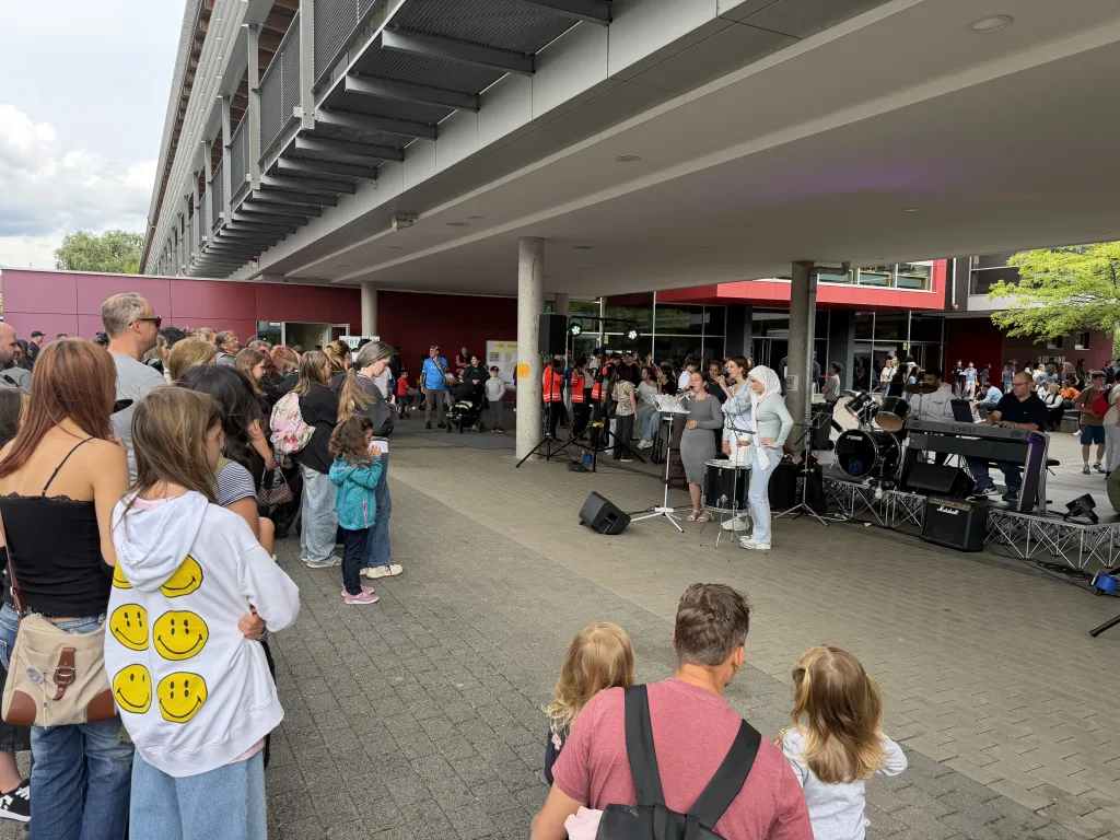 Viele Gäste stehen im überdachten Gang am Schulhof.