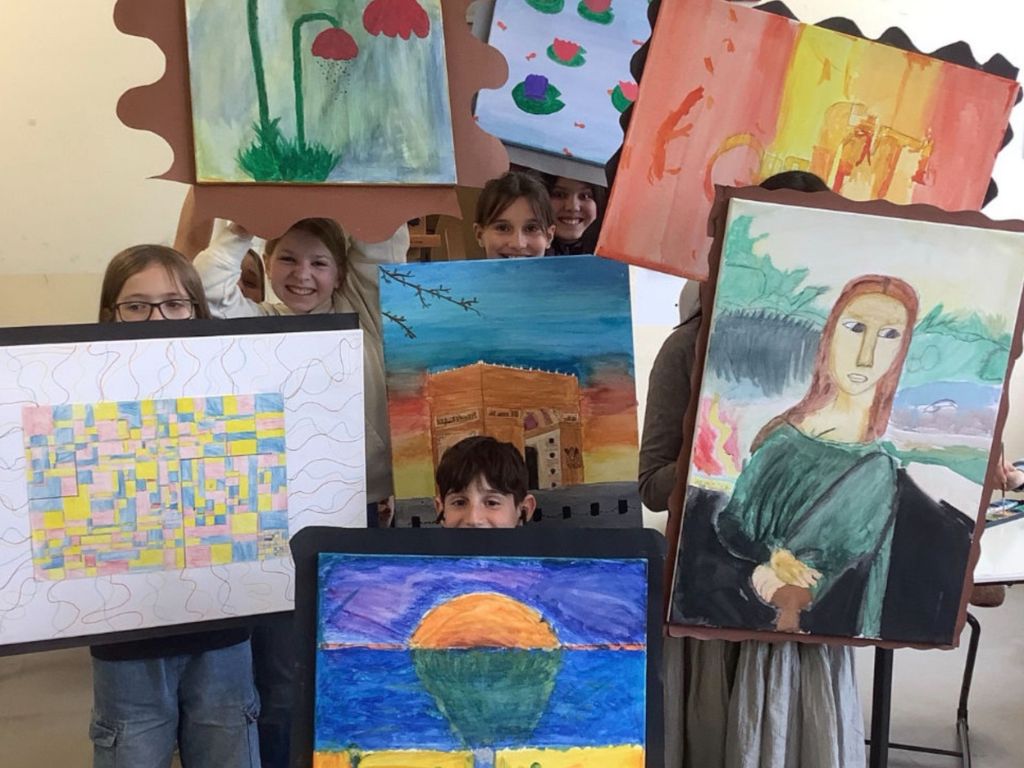 Mehrere Kinder halten selbst gemalte Bilder hoch – darunter ein Porträt im Stil der Mona Lisa, abstrakte Muster und Landschaften.