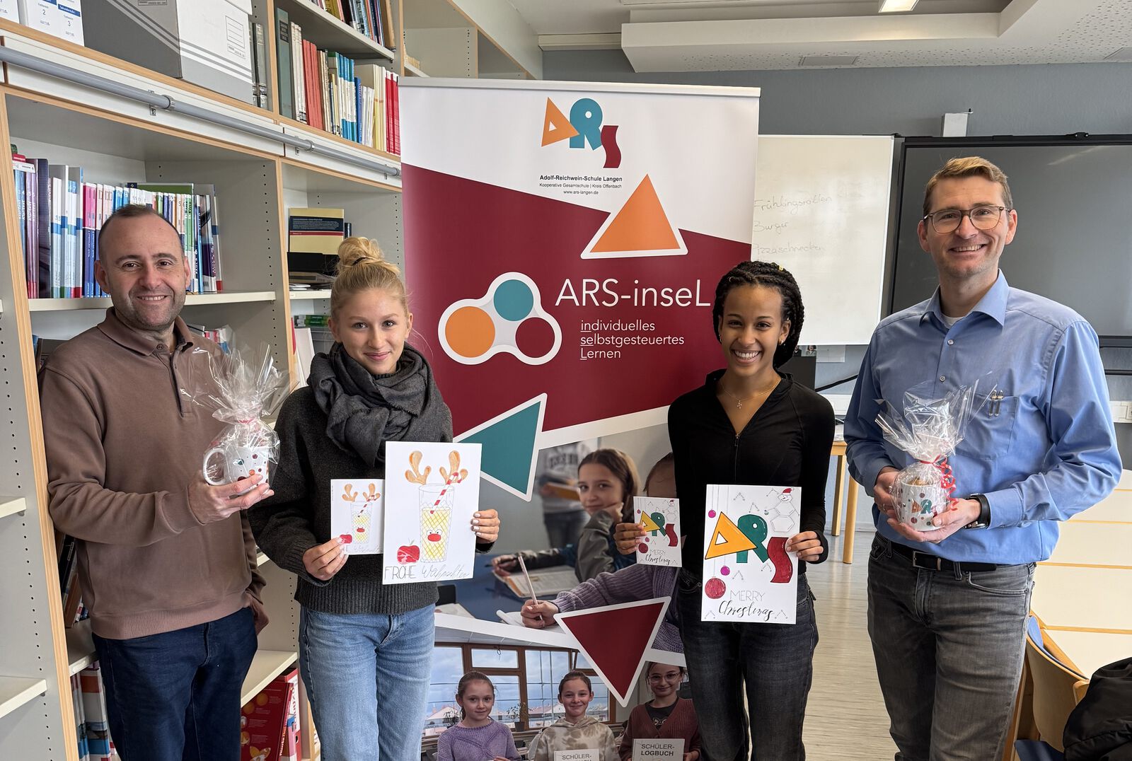 Zwei Jugendliche halten selbst gestaltete Weihnachtskarten, daneben zwei Erwachsene mit eingepackten Geschenken; im Hintergrund ein Roll-up mit der Aufschrift „ARS-inseL – individuelles selbstgesteuertes Lernen“.