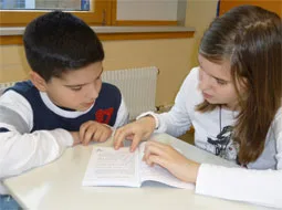 Zwei Kinder sitzen nebeneinander und lesen gemeinsam in einem Text.