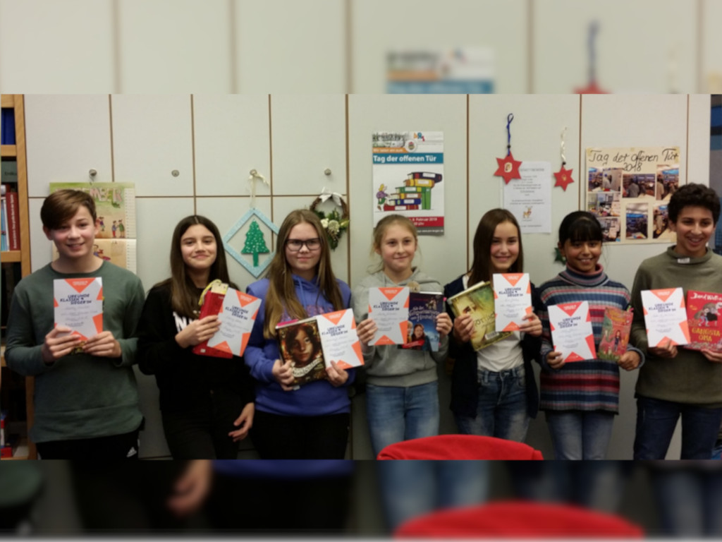  Schüler und Schülerinnen halten Bücher und Urkunden hoch 