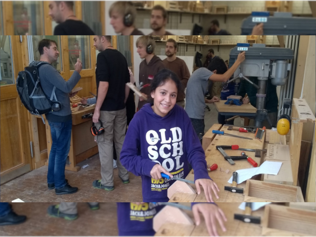 Die Schülerin blickt in die Kamera, während sie Holz schleift.