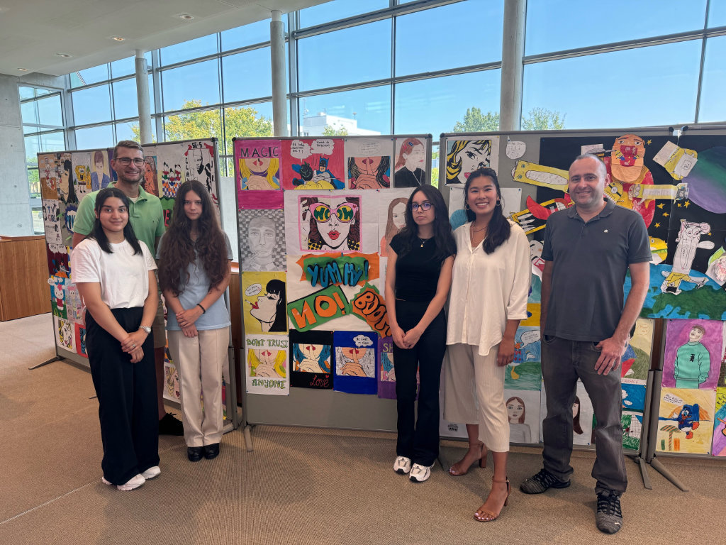 Drei Schülerinnen eröffnen mit den verantwortlichen Lehrkräften, Frau Nguyen und Herrn Matschek-Marian (rechts), und Herrn Becker (links) die Kunstausstellung. Drei Schülerinnen stehen mit den verantwortlichen Lehrkräften, Frau Nguyen und Herrn Matsche-Marian, und Herrn Becker vor den Kunstwerken.