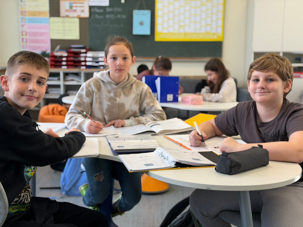 Drei Kinder arbeiten an Gruppentischen im Klassenraum an ihren Aufgaben